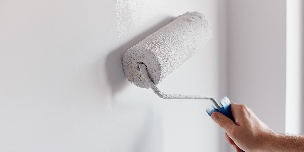 Male hand painting wall with paint roller. Painting apartment, renovating with white color paint